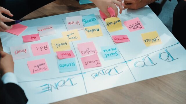 Close up of professional business team hands writing and putting sticky note on scrum task board. Top view of project manager write task and use kanban board to manage time and workflow. Directorate.