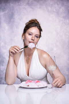 A woman is about to eat a flower speared on a fork. Female surreal portrait with floral dinner.