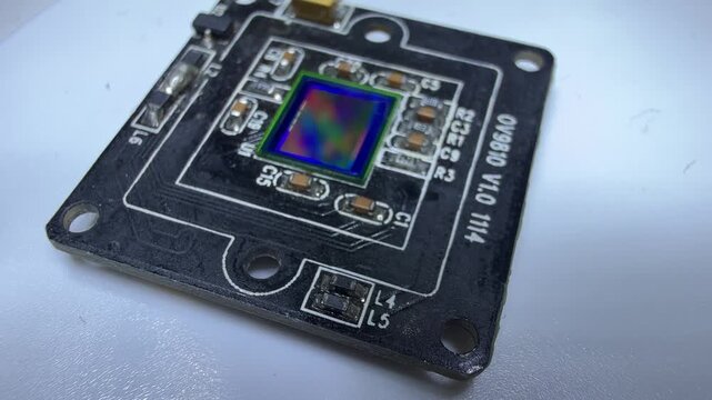 Macro shot of a camera module circuit board with an iridescent image sensor on a white surface