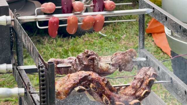Argentine asado rotating grill with beef cuts and sausages roasting over heat, showing browned meat, fresh sausage and rotating barbecue equipment outdoors