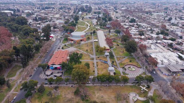 Drone shot of Parque General Belgrano in San Juan showcases geometric walkways, modern buildings, lush trees, and an expansive urban landscape under overcast skies.