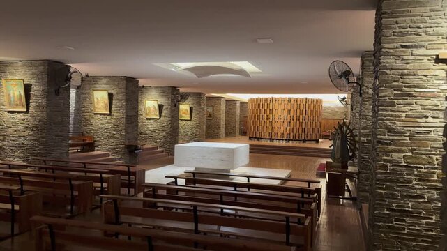 Catedral de San Juan Bautista crypt with rustic stone walls, wooden screen, altar and timber benches, reflecting restrained modern religious architecture, San Juan, Argentina, camera pan