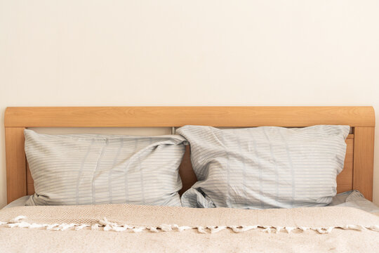 Cozy bedroom interior featuring a wooden headboard, light blue striped pillows, and textured throw blanket against plain white wall. Slow living, mindful consumption