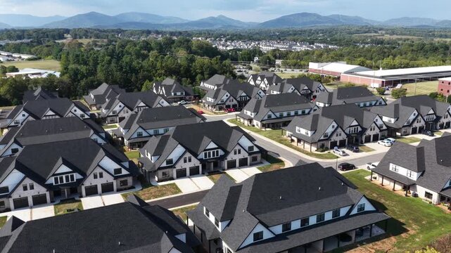 Westyn Village townhomes line curving streets in Forest, Virginia, with dark pitched roofs, pale gabled facades and garages below distant wooded hills. Aerial view