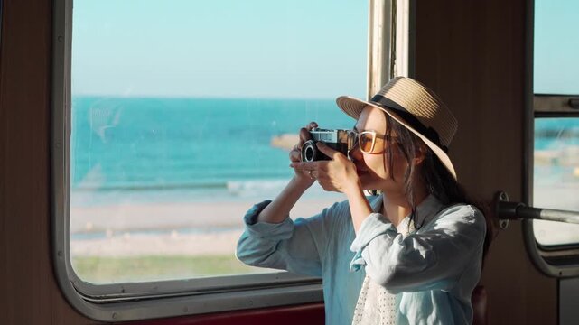 Solo female traveler taking pictures of sea view while traveling by train on summer vacation