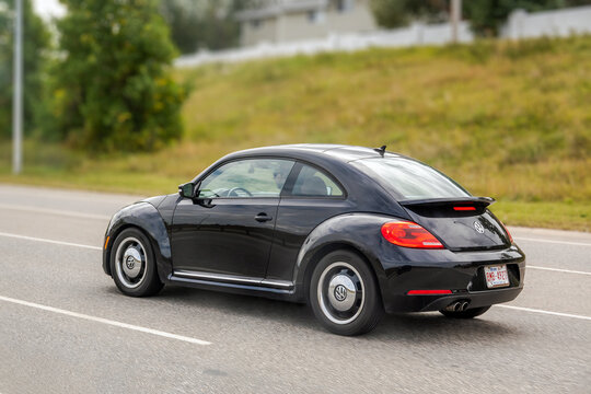 Calgary, AB, Canada. September 29, 2026. Three-quarter rear view of a black Volkswagen Beetle car driving on a suburban asphalt road.