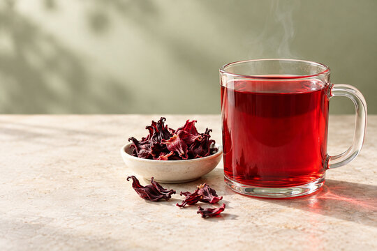 Roter Hibiskustee im Glas mit getrockneten Hibiskuskelchen