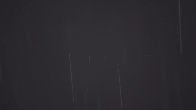 黒い住宅の外壁を背景に美しく降り注ぐ雨粒と雨筋を捉えたスローモーション映像。ピント位置のバリエーション