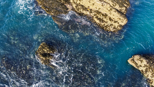 Aerial view of clear turquoise sea water washing over submerged and exposed rocky reef