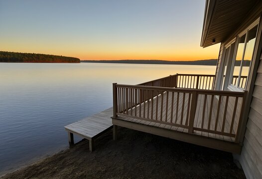 A lakeside cabin with a wooden deck overlooking the water, warm evening light