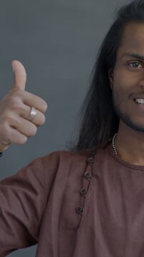 Portrait of happy Indian man showing thumbs-up hand gesture smiling looking at camera on black studio background. People and positive emotion concept.