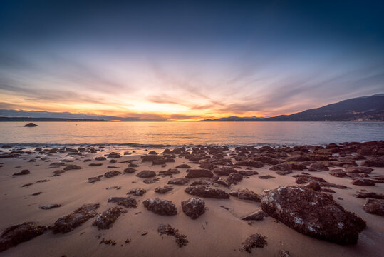 Sun rays fanning across the sky over a rocky beach at sunset, English Bay, Vancouver, British Columbia, Canada