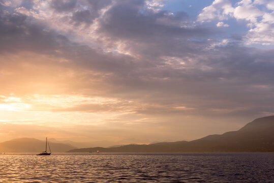 Dramatic clouds over a calm inlet with a sailboat and mountains at sunset, Vancouver, British Columbia, Canada