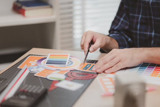 Designer working with color palettes, layout templates, and creative design tools on a desk while planning branding and graphic design projects in a modern office.