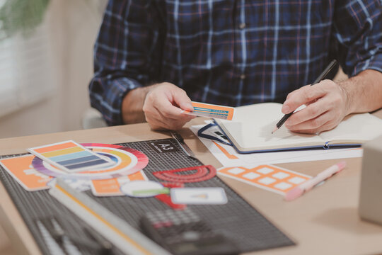 Designer working with color palettes, layout templates, and creative design tools on a desk while planning branding and graphic design projects in a modern office.