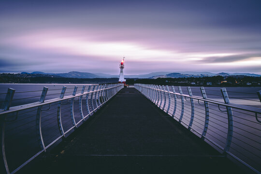 Long pier to the lighthouse with railings stretching into calm water at dusk under a purple sky, Victoria, BC, Canada