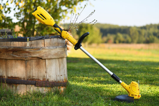 Yellow string trimmer on green grass outdoors near a wooden barrel