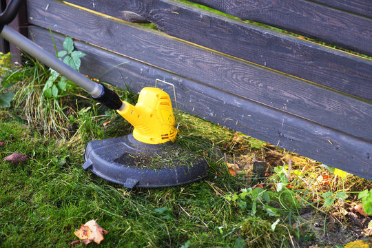 Trimming grass along a wooden fence with a string trimmer 