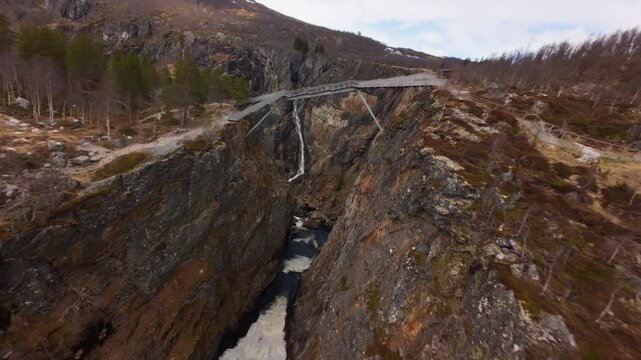 FPV drone flies over the gorge and passes beneath a bridge while approaching Voringfossen waterfall in Norway.
