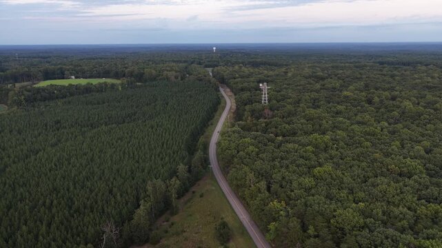A road and communications tower border wooded land sold for a planned data center in Louisa County, Virginia, with a distant water tower above the trees. Aerial view