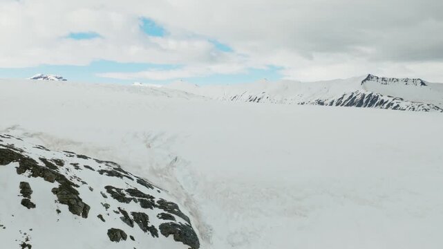 Snow covered glacial terrain in the Icelandic Highlands, Iceland, with broad ice-covered slopes, exposed dark rock and a rugged mountain ridge, aerial