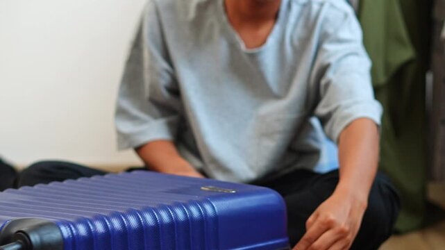 Close-up of hands unzipping blue travel suitcase placed horizontally on wooden floor