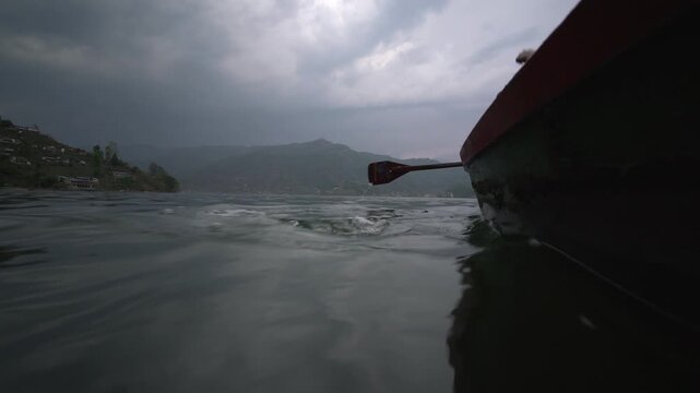 A wooden oar paddles a boat across choppy water on Phewa Lake beneath a stormy sky in Pokhara