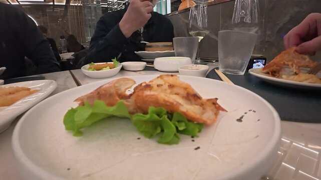 Pan fried Chinese dumplings served with lettuce on ceramic plates at a Chinese restaurant, with diners using chopsticks and sharing dishes across the table, close up