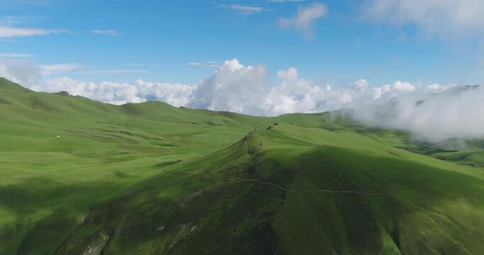 Drone shot of Badimalika, Bajura, Nepal, of a prominent green ridgein high altitude valley with low monsoon clouds drifting over rolling pastures under clear blue skies in Tribeni Patan
