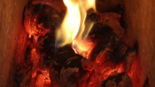 Fire and flames are burning and flickering in a wood stove fireplace with glowing wood logs.