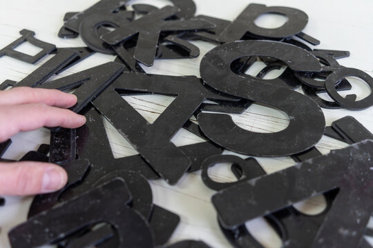 Manually laying out large black letters of the alphabet on lined paper. Milling letters made of plastic on a machine.Production of advertising.