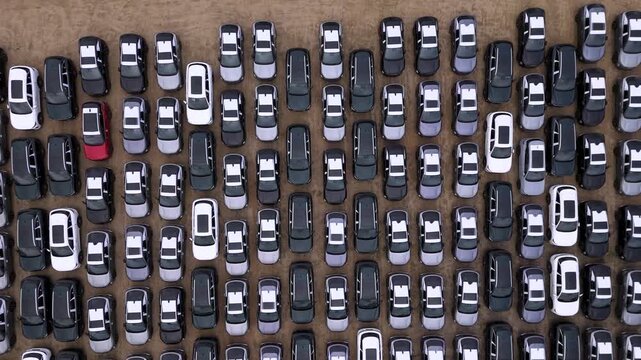 High-angle aerial drone view showing rows of brand new modern vehicles stored at a distribution logistics hub. The visual represents industrial supply chain management, automotive manufacturing, and g