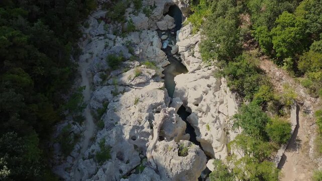 Aerial view of sculpted rocks along Acheron River in Greece. Water runs through a narrow channel between pale boulders, with dense vegetation and a footpath beside the gorge.