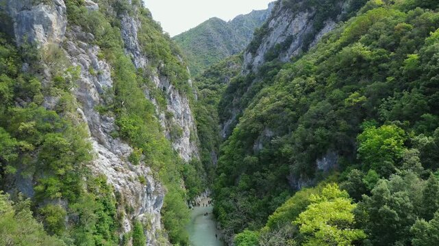 Drone flies forward through Acheron River gorge between wooded cliffs in Greece