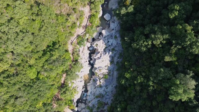 Drone flies forward above rocky Acheron River channel between trees in Greece