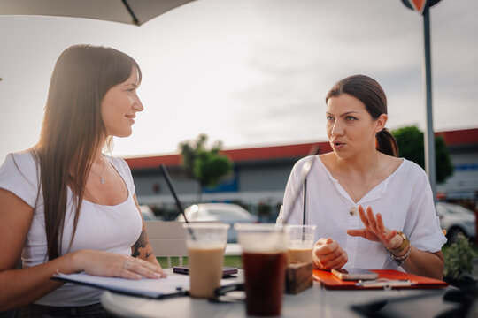 Women discussing work at outdoor cafe during sunset