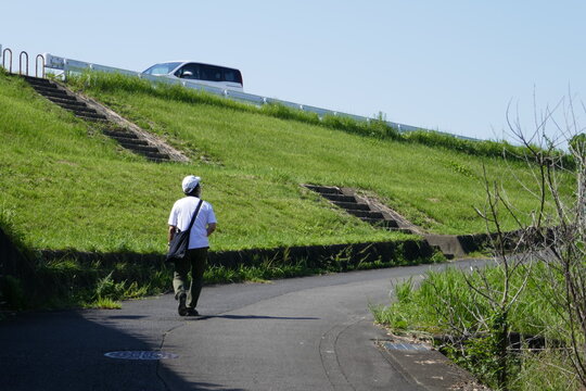 晴れた日に坂下の道を歩く男性の後ろ姿