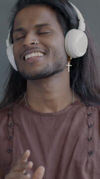 Portrait of happy Indian man listening to music with headphones dancing having fun on black background. People and modern technology concept.