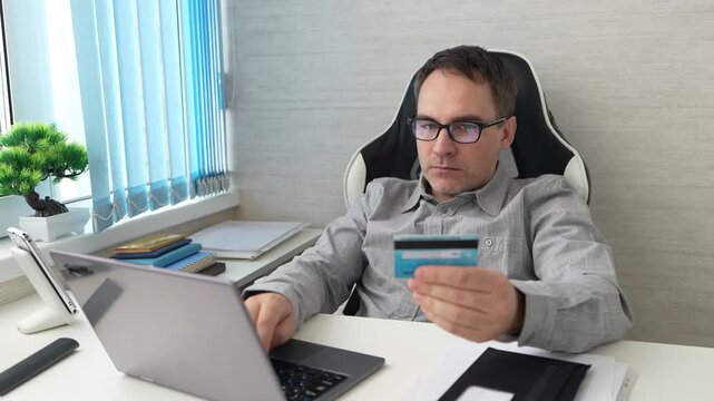 Businessman entering bank card data into laptop, online payment, financial transaction at desk.