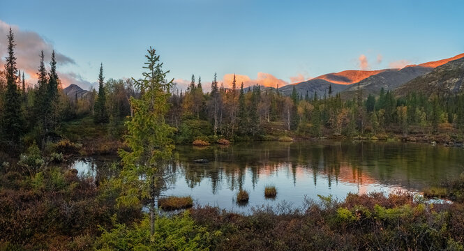 Sunset landscape of Khibiny mountains with mountain lake reflection, colorful autumn taiga forest and soft evening light, Kola Peninsula, Arctic Russia.
