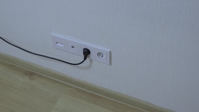Wall power outlet with connected electrical cable in a residential interior, representing home electricity, power supply and modern electrical installation