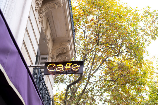 Cafe sign on a traditional building facade beside golden autumn trees, combining everyday city life, seasonal foliage and a warm urban street atmosphere