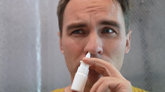 Man using a nasal spray to treat a stuffy nose and congestion, looking at the camera. Allergy relief, sinus treatment, and cold symptoms.