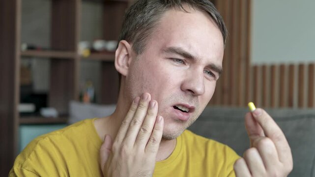 Sick man holding pills in hand, trying to swallow one, health treatment at home. analgesic for toothache.