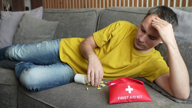 Man holding his head and yellow pills, expressing severe headache and discomfort. Concept of migraine, tension headache, pain relief, and medication.