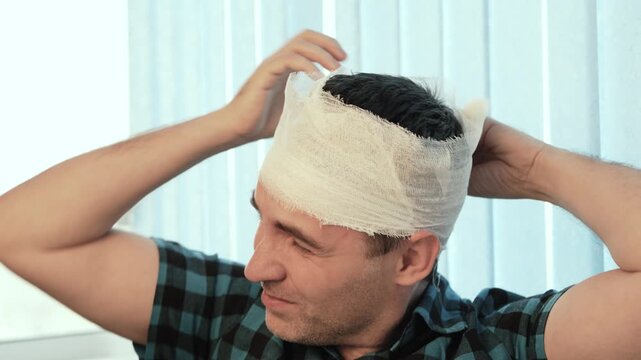Injured man bandaging his own head, wound care and self-treatment.
