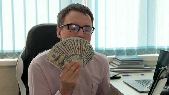 Businessman holding fan of hundred-dollar bills and smelling money. High profit, salary, and financial success in cash.