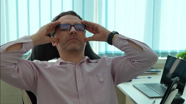 Tired businessman touching his forehead while sitting at his desk, clearly exhausted and bored. Professional burnout, work fatigue, and long office hours.