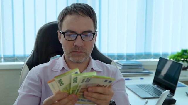 Focused businessman holding a stack of euro banknotes in an office, seriously thinking about his finances, income, profit, or a business decision.