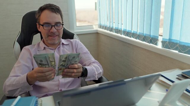 Satisfied businessman holding a stack of US dollar bills in an office, celebrating a salary payment, business profit, or successful contract deal.